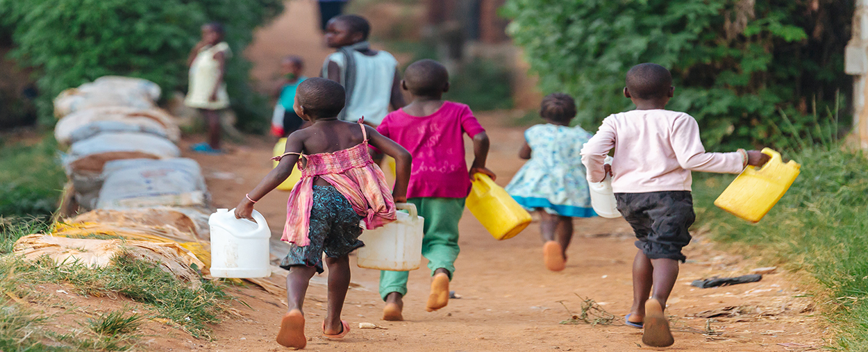 A stock photo of a group of children carrying jugs to collect water.