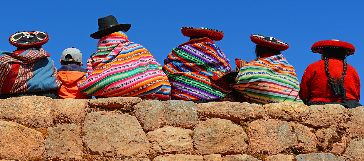 This is a stock photo. A Quechua family sitting on a ledge looking out. 